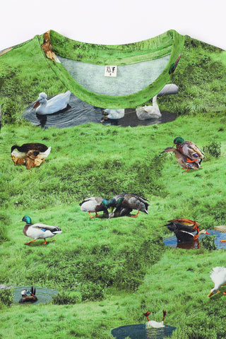 Green shirt with printed design of ducks in a field and pond.