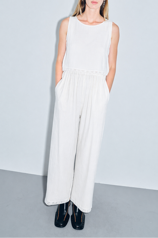 Woman wearing a white sleeveless top and wide-leg pants against a plain background